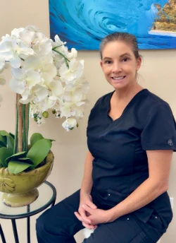 Hillary, Dental Hygienist, seated in navy scrubs beside an orchid at Tropical Smiles Dental